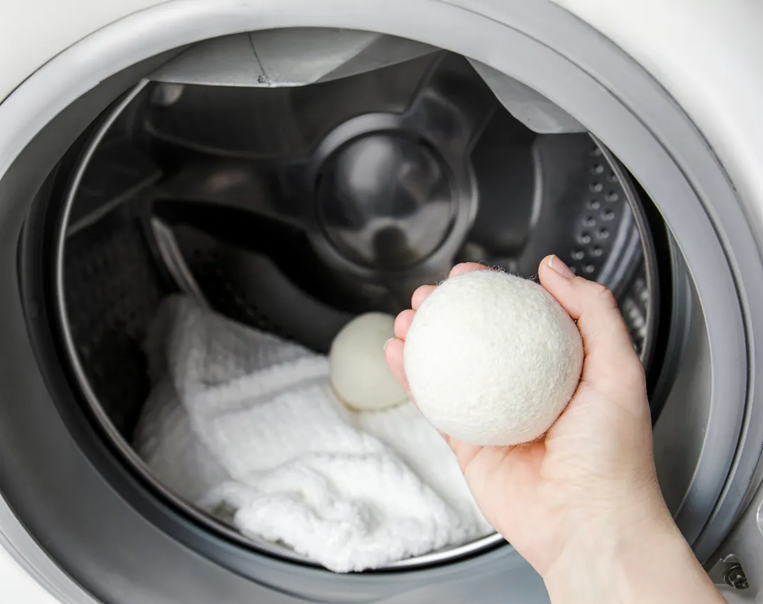 Placing a wool dryer ball into a drum of fresh white laundry