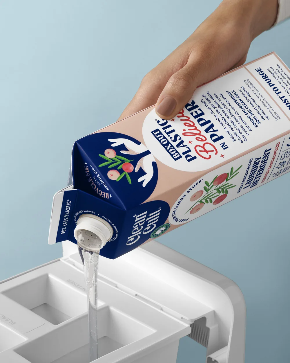 A close-up of Juniper Sandalwood detergent pouring from its carton into a washer's dispenser drawer
