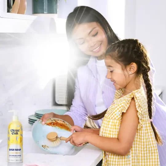 A mother and daughter washing dishes together at a bright kitchen sink