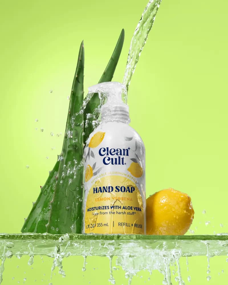 A bottle of hand soap in a splash of water with aloe leaves and a lemon