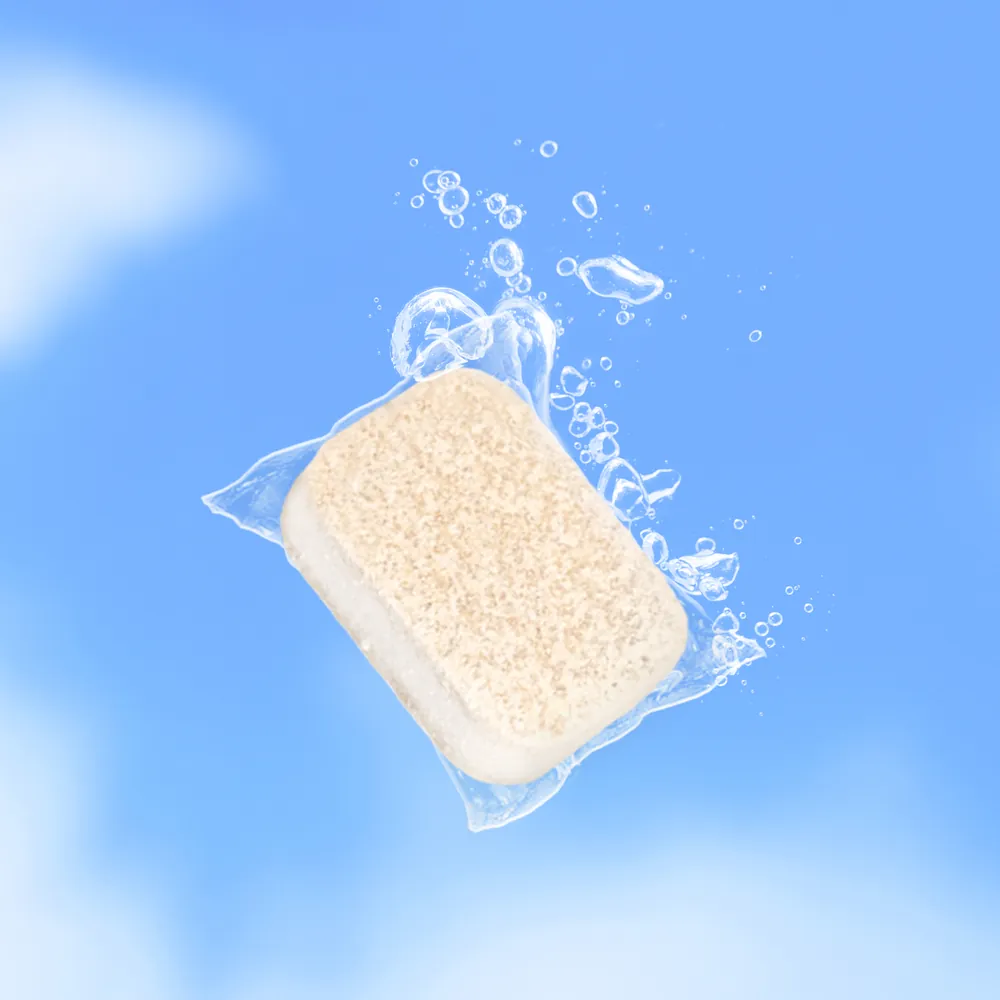 A dishwasher tablet in its clear film, fizzing in water against a blue sky